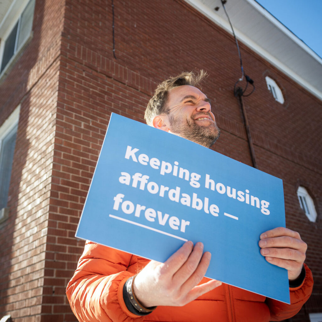 Man holding a sign that reads "keeping housing affordable– forever."